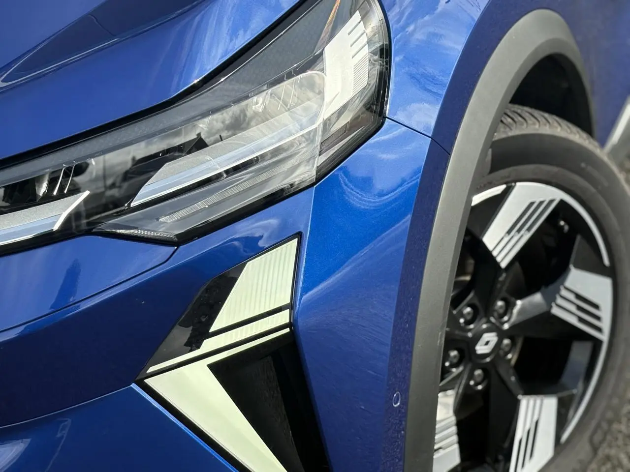 Gros plan sur l'avant droit bleu Iron du Renault SYMBIOZ, mettant en valeur le phare LED et la jante 18" Gravity.