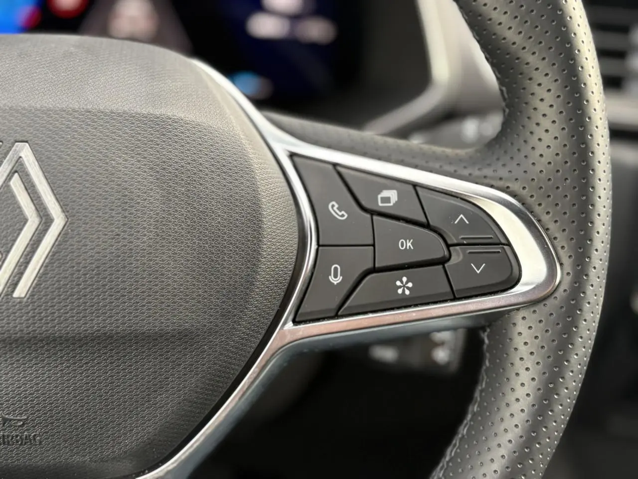 Gros plan sur le volant en cuir perforé du Renault Symbioz bleu, avec commandes multifonctions et logo central.