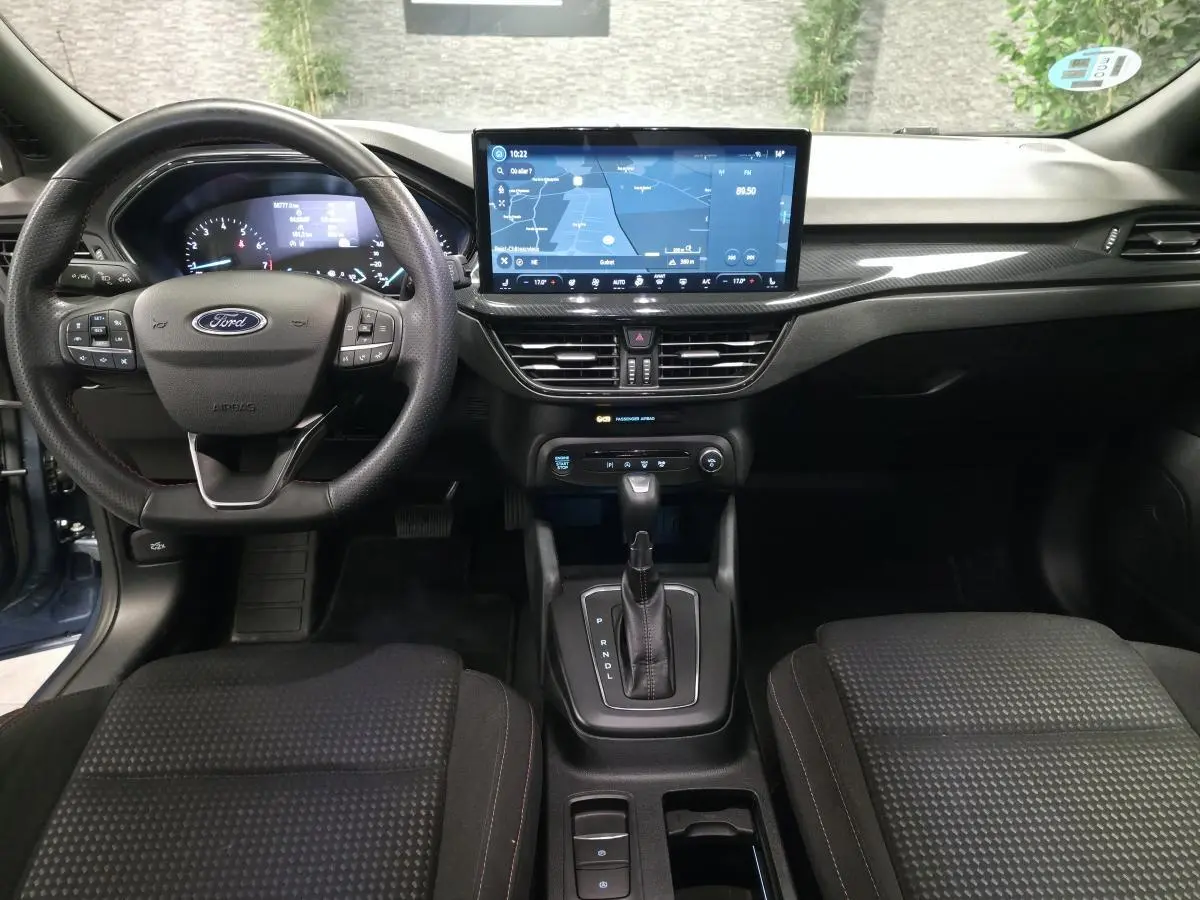 Vue intérieure avant de la Ford Focus 2024 bleu, volant ST Line, écran tactile central et levier de vitesses automatique.