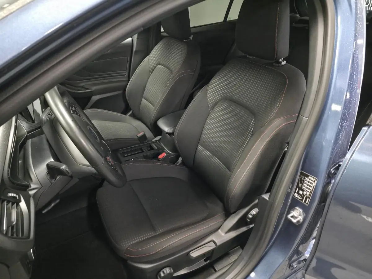 Vue intérieure côté conducteur de la Ford Focus 2024 bleu azur, sièges tissu ST-Line avec surpiqûres rouges et volant trois branches.