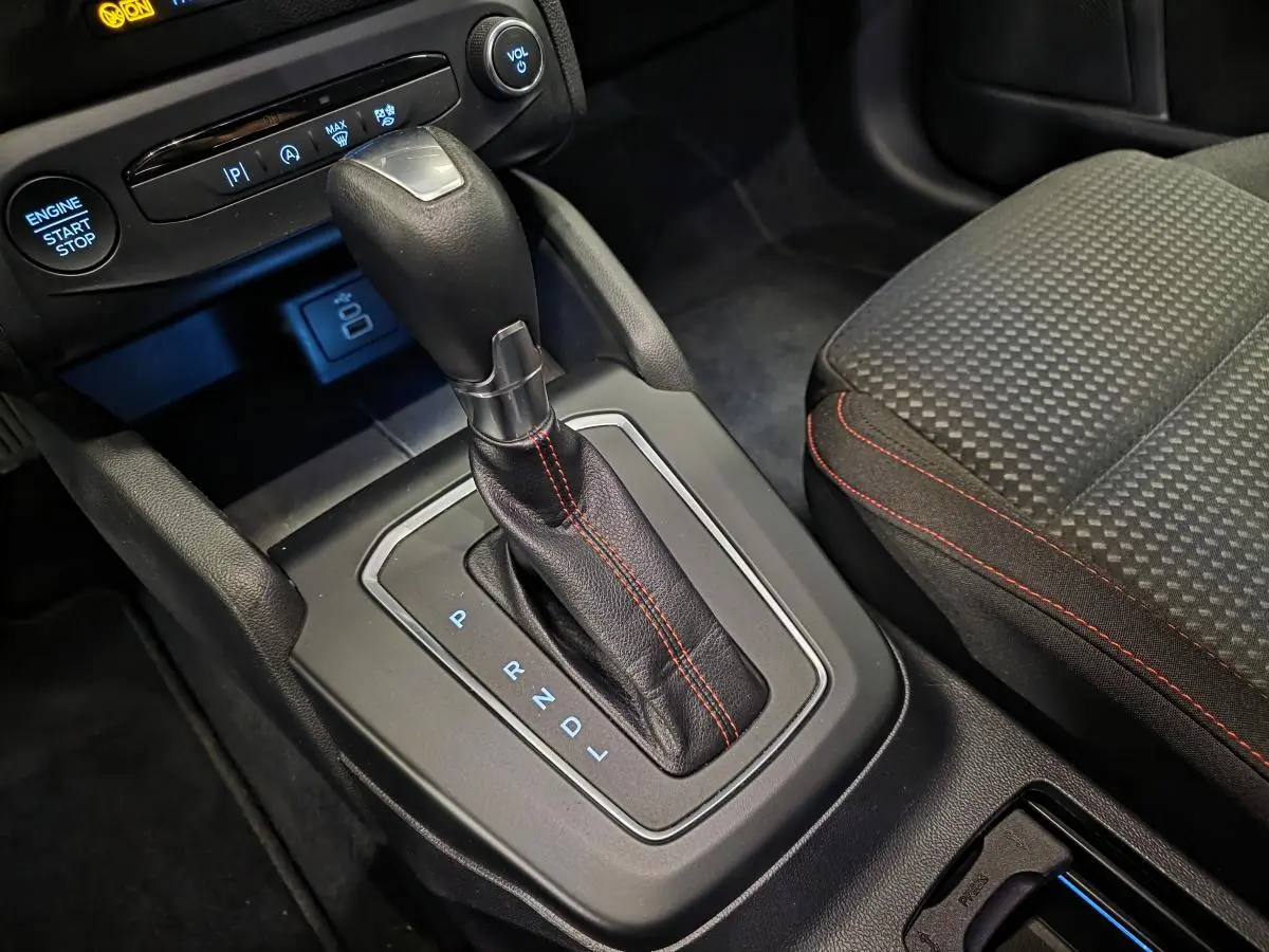 Gros plan sur la console centrale de la Ford Focus 2024 ST Line, levier de vitesses automatique avec surpiqûres rouges et siège tissu à motifs.