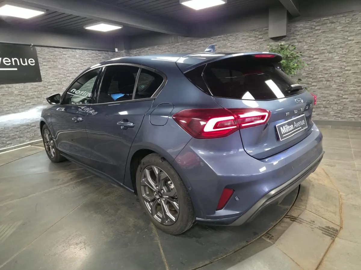 Vue 3/4 arrière droite d'une Ford Focus 2024 bleu métallisé avec feux arrière LED et jantes alliage 17 pouces.