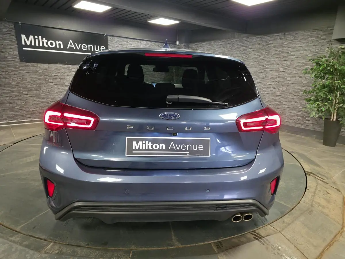 Vue arrière d'une Ford Focus 2024 bleu azur avec feux LED allumés et double sortie d'échappement sport.