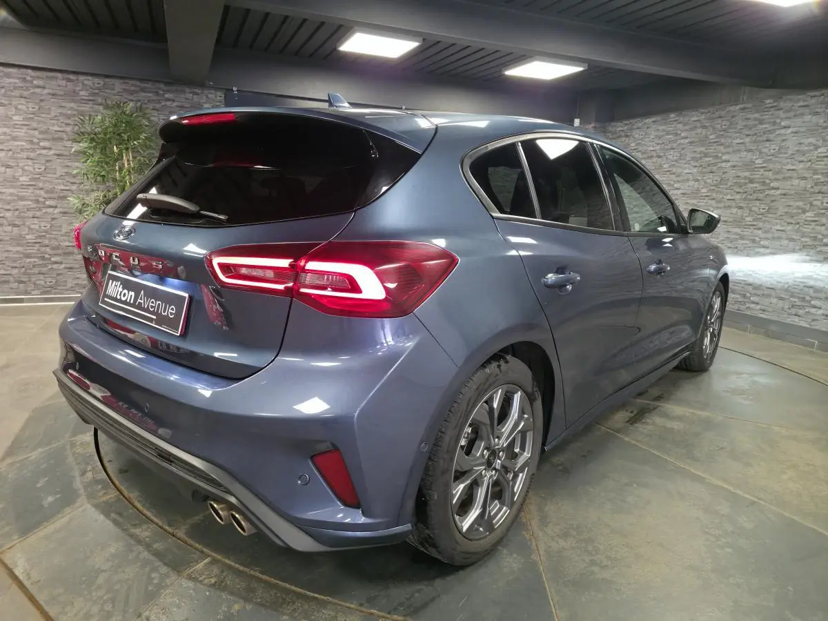 Vue 3/4 arrière droite d'une Ford Focus 2024 bleu métallisé avec feux arrière LED et double sortie d'échappement sport.