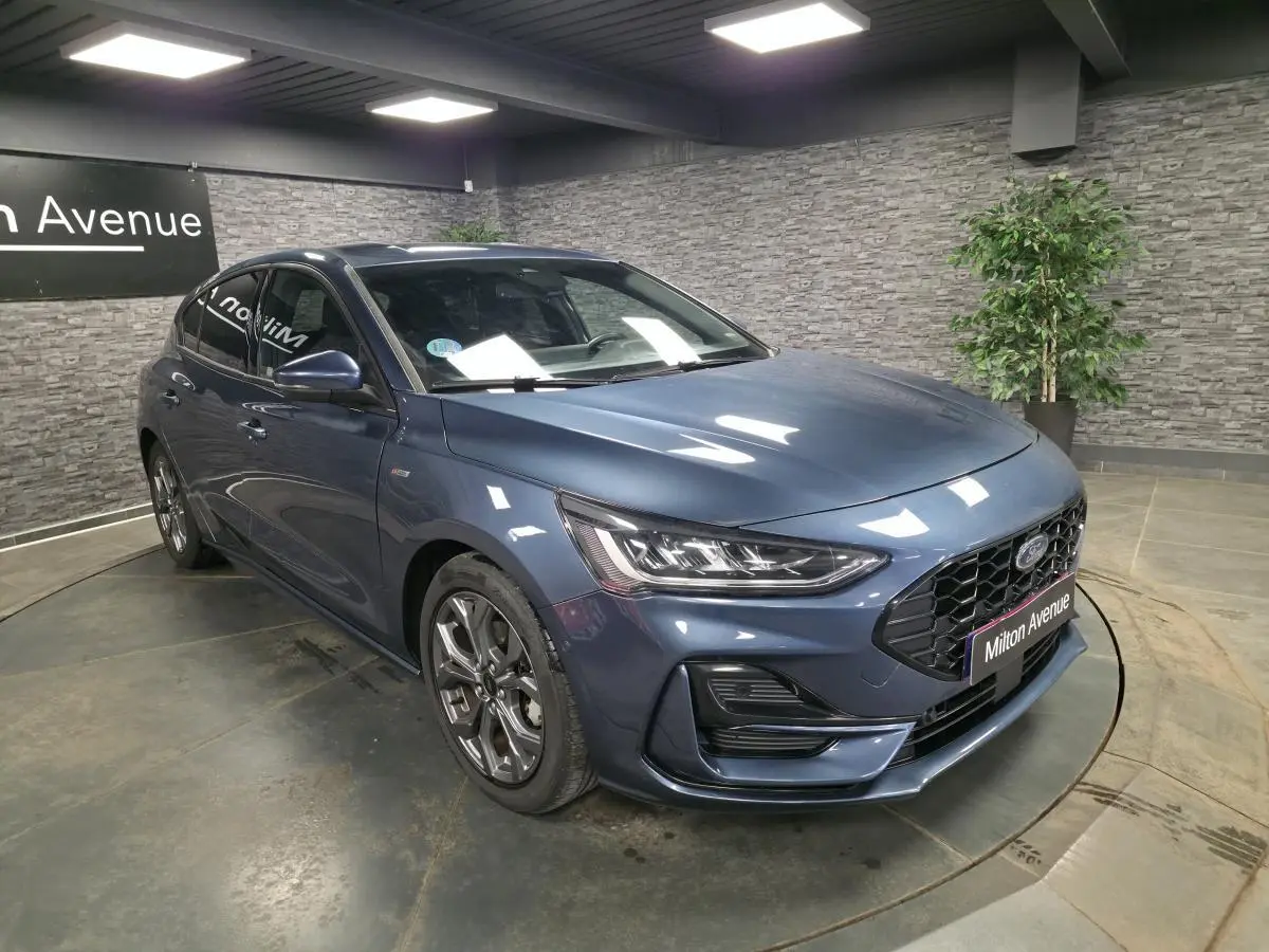 Ford Focus 2024 bleu métallisé vue 3/4 avant avec calandre noire et jantes alliage 17 pouces dans un showroom.