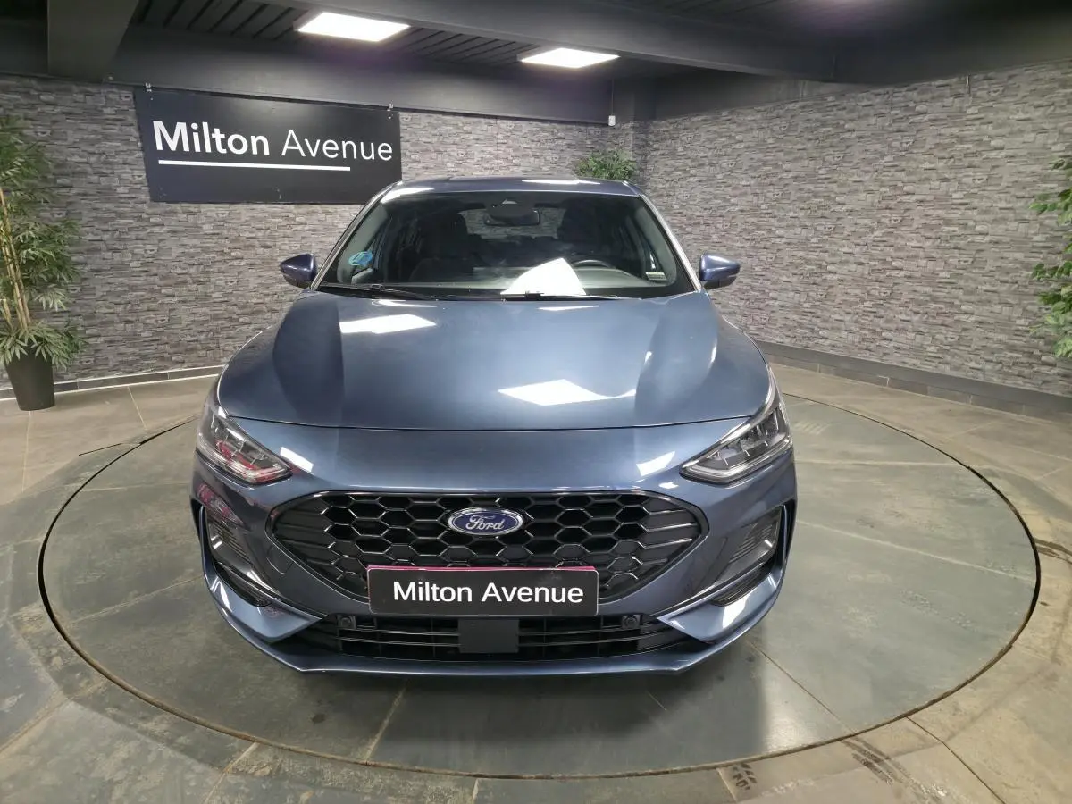 Vue avant d'une Ford Focus 2024 bleu métallisé avec calandre noire ST-Line et phares LED, en intérieur showroom.