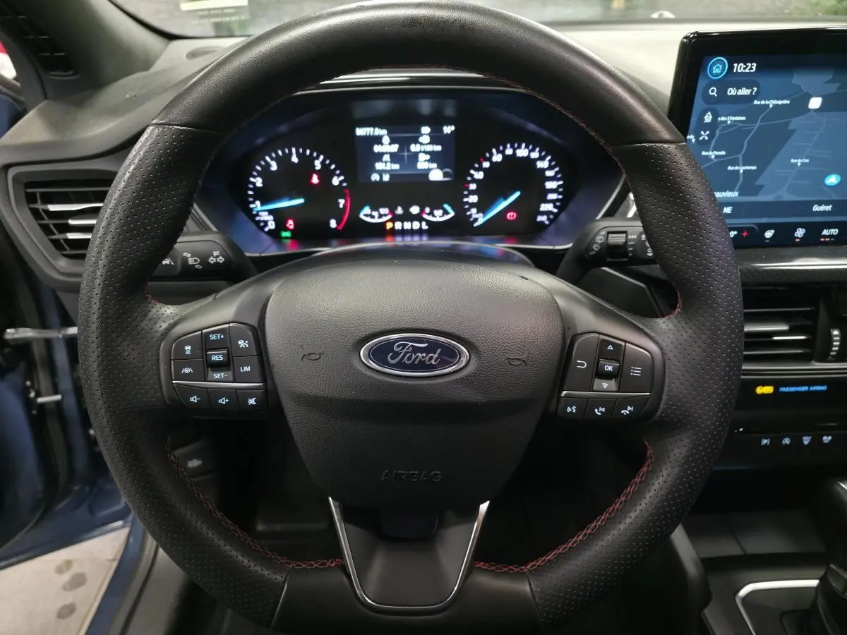 Vue intérieure centrée sur le volant ST-Line en cuir noir avec surpiqûres rouges et tableau de bord numérique de la Ford Focus 2024.