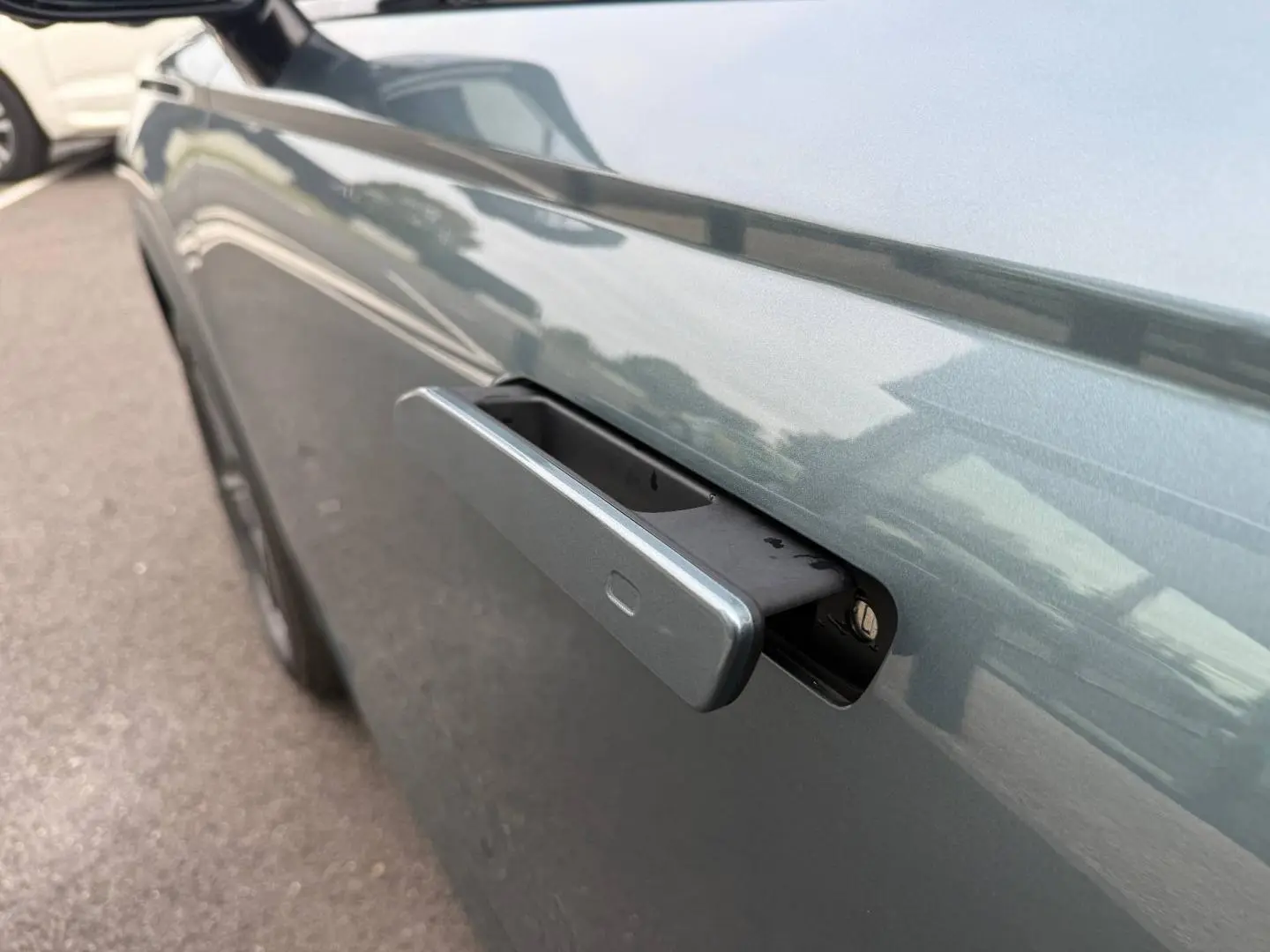 Poignée de porte rétractable côté gauche d'une JAECOO J7 Olive Grey Métal avec reflet du toit Carbon Crys Black.