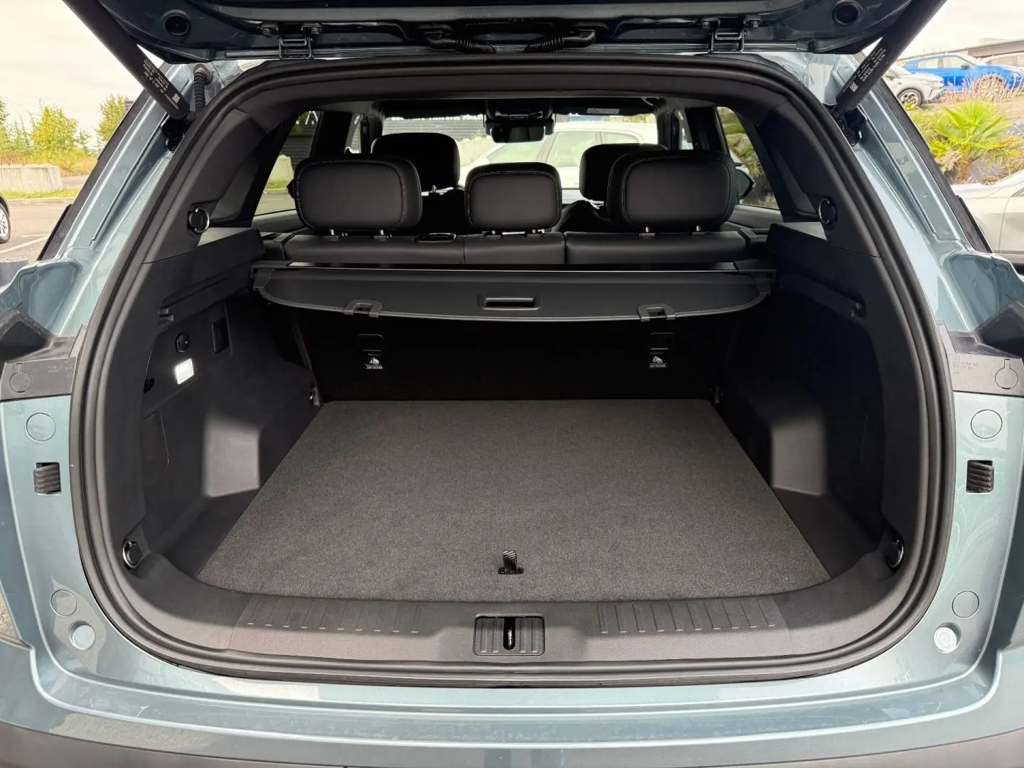 Coffre ouvert vu de l'arrière d'un JAECOO J7 olive grey métal avec intérieur noir et cache-bagages.