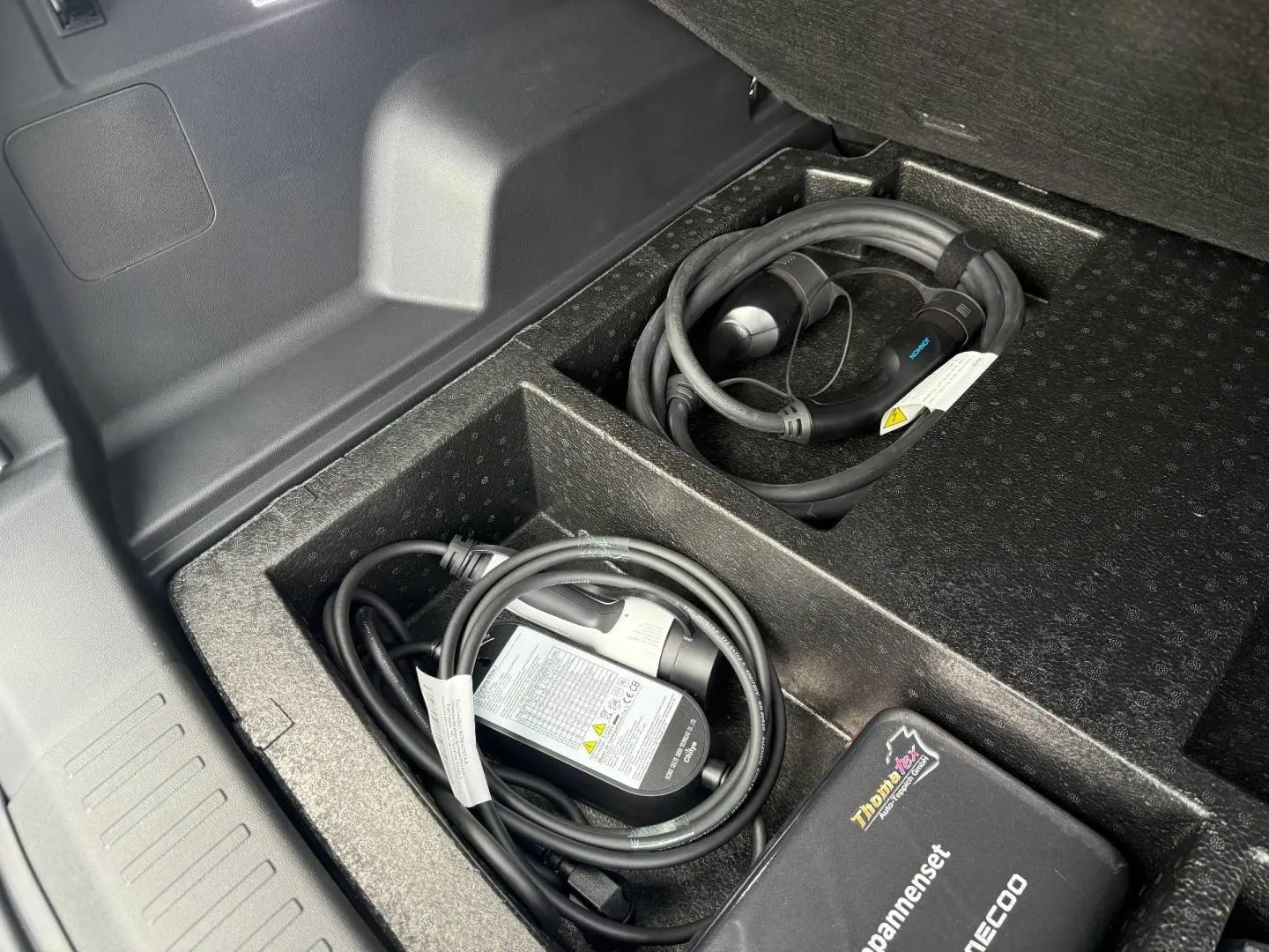 Coffre ouvert du JAECOO J7 hybride, montrant le rangement noir avec câbles de recharge et accessoires.