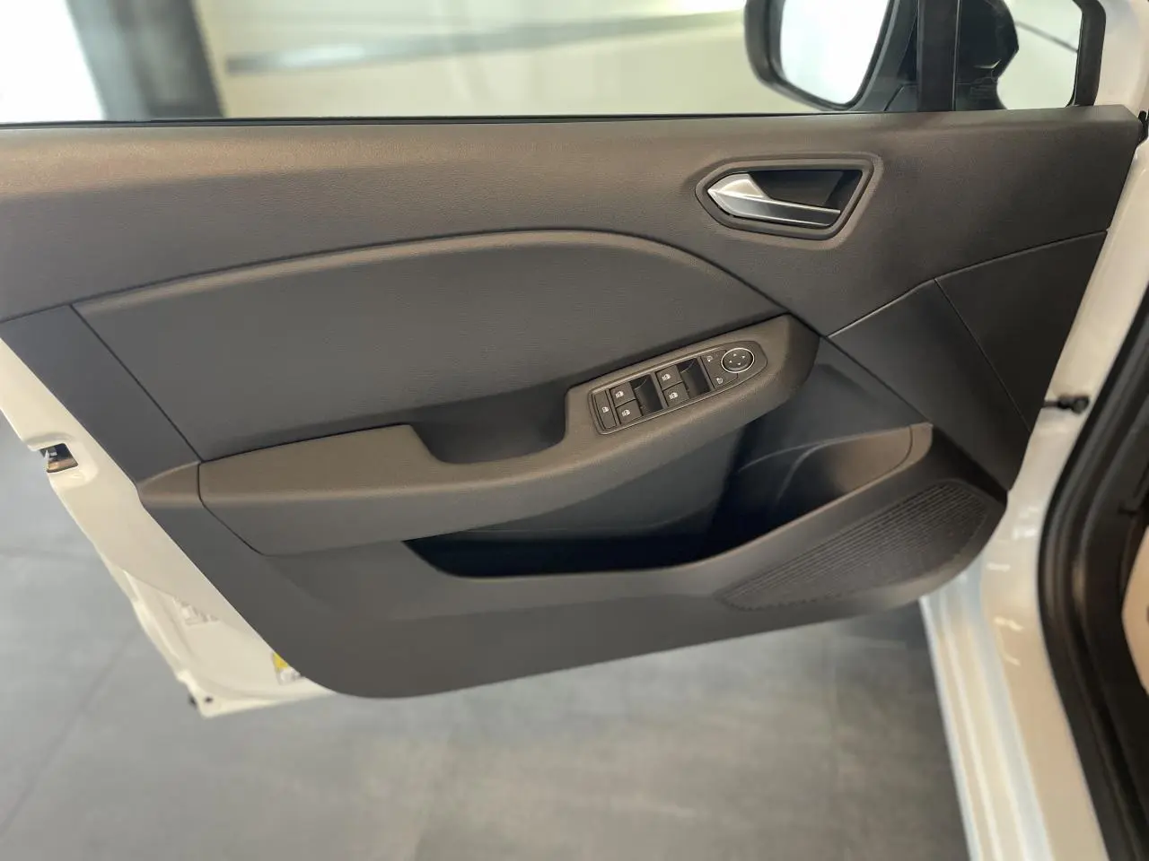 Porte avant gauche ouverte d'une Renault Clio blanche, montrant la garniture noire avec commandes électriques des vitres.