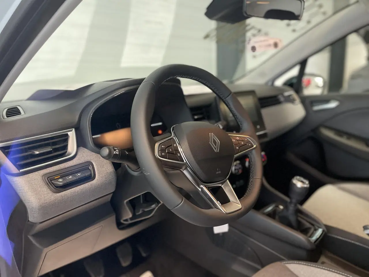 Intérieur de la Renault Clio 2025, vue côté conducteur sur le volant multifonction et la console centrale avec levier manuel.