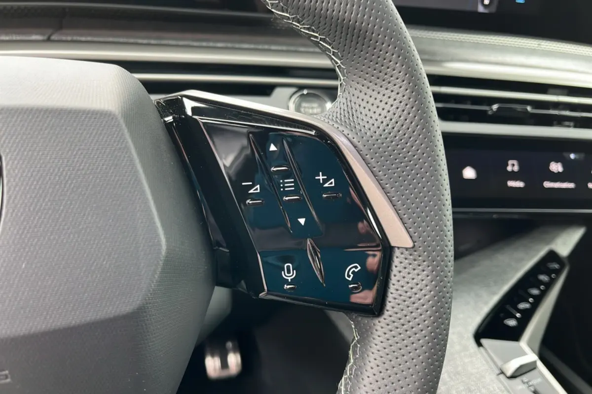 Gros plan sur les commandes multifonctions du volant cuir perforé du Peugeot 5008 Hybrid gris titane.