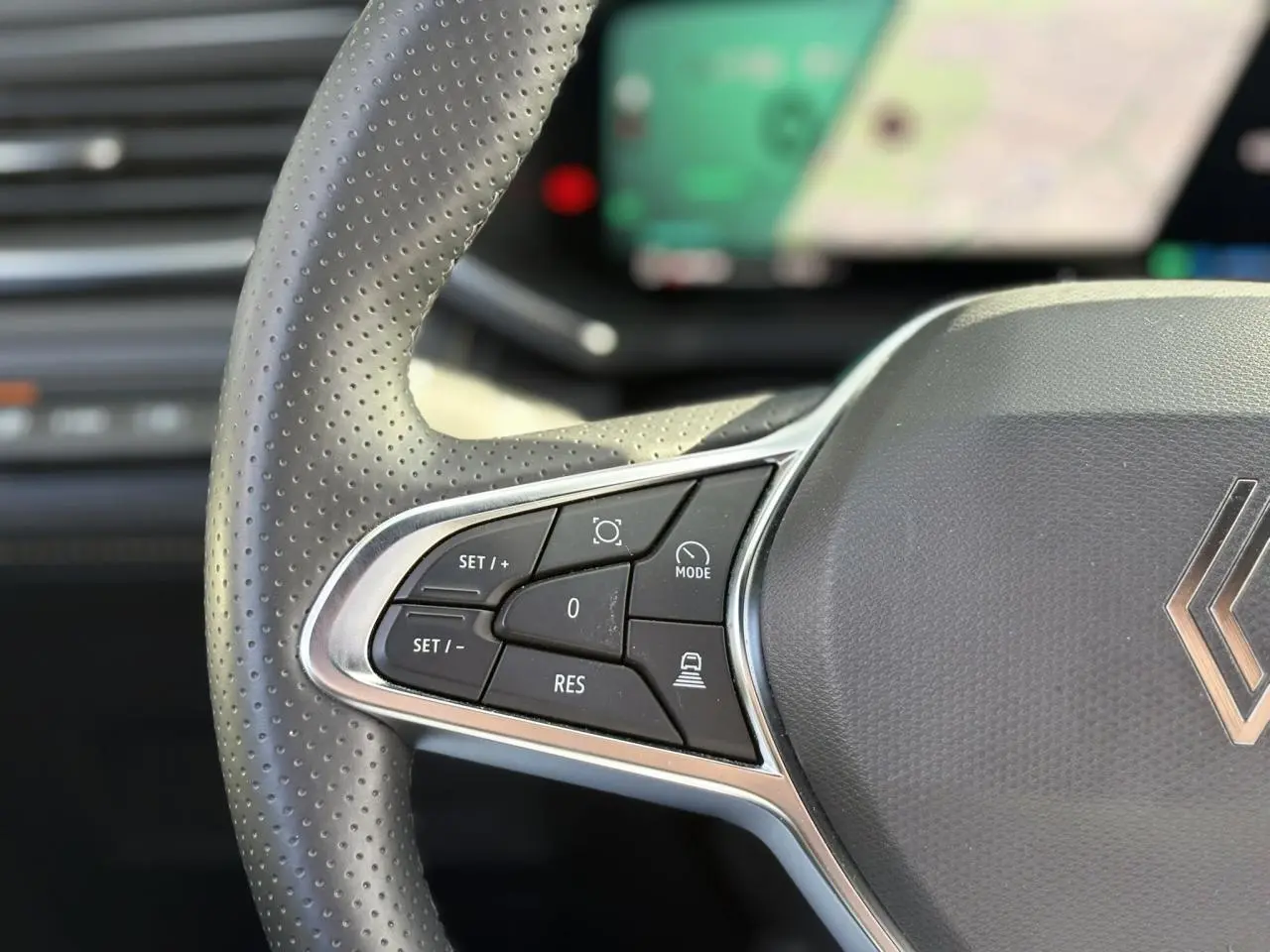 Gros plan sur les commandes du volant en cuir perforé gris du Renault Symbioz 2025 avec affichage numérique flou en arrière-plan.