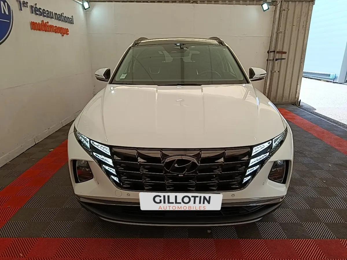 Vue frontale d’un Hyundai Tucson blanc 2022 avec calandre noire et feux LED distinctifs, en intérieur showroom.