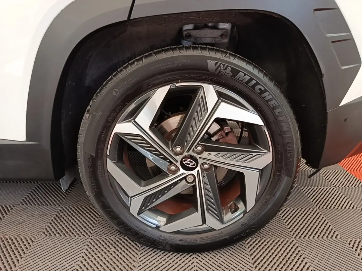 Gros plan sur la roue avant droite blanche du Hyundai Tucson 1.6 Hybrid 230 Executive avec jante alliage moderne.
