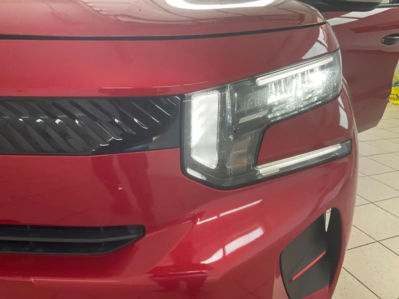 Gros plan sur l'avant droit rouge métallisé du Citroën C3 ë-113 Berline Max 2025, mettant en valeur son phare LED distinctif.