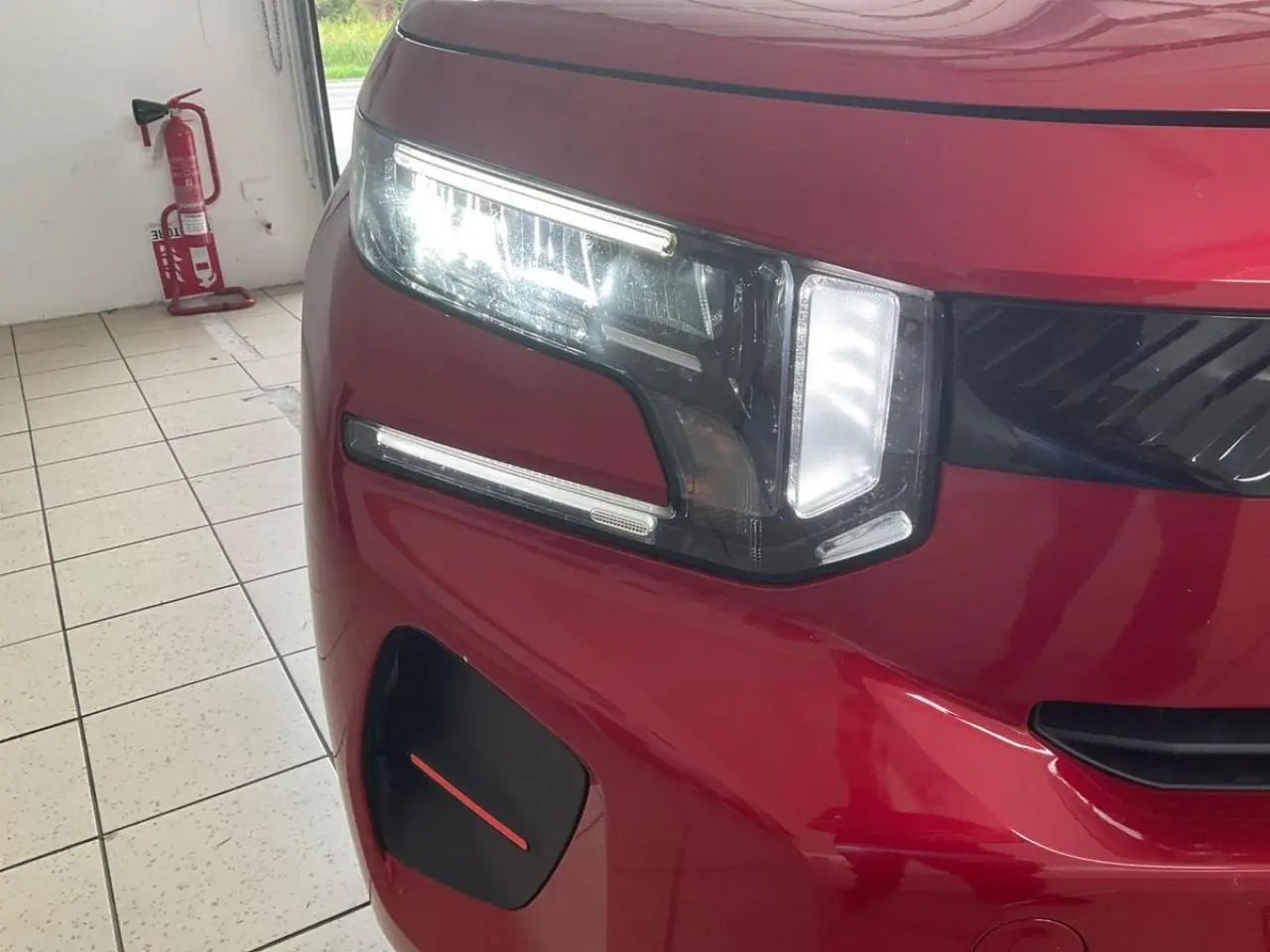 Gros plan sur l'avant gauche de la Citroën C3 ë-113 Berline Max 2025 en rouge métal foncé avec phares LED allumés.