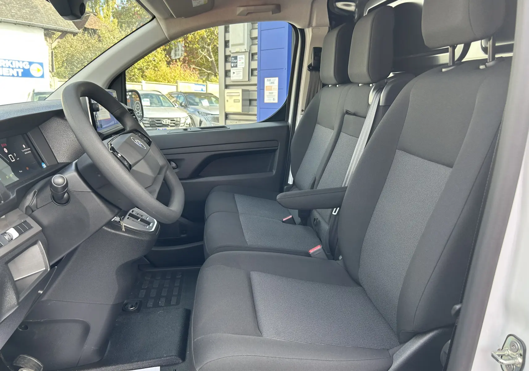 Vue intérieure côté conducteur du Citroën Jumpy blanc 2025, montrant les sièges tissu gris et le tableau de bord moderne.