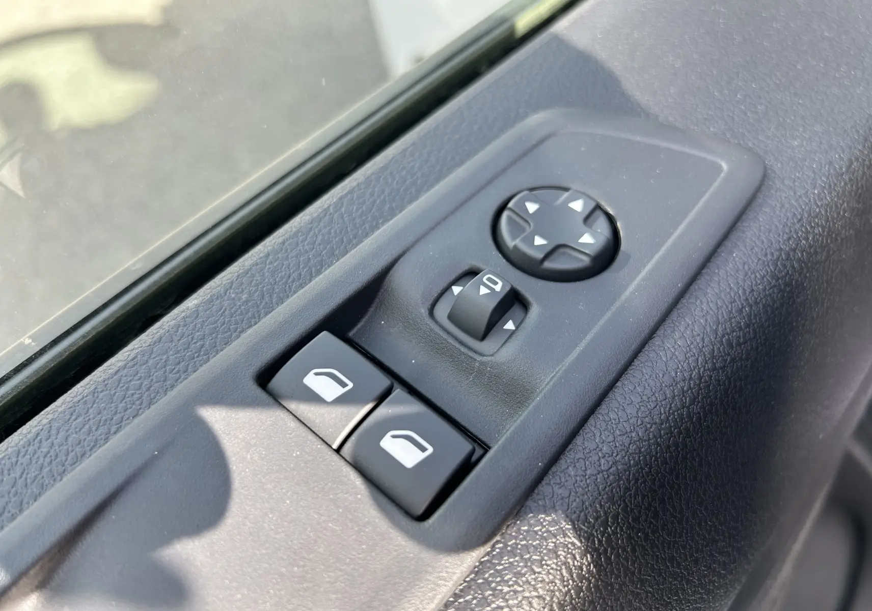 Gros plan sur les commandes de réglage des rétroviseurs et des vitres côté gauche du Citroën Jumpy blanc.