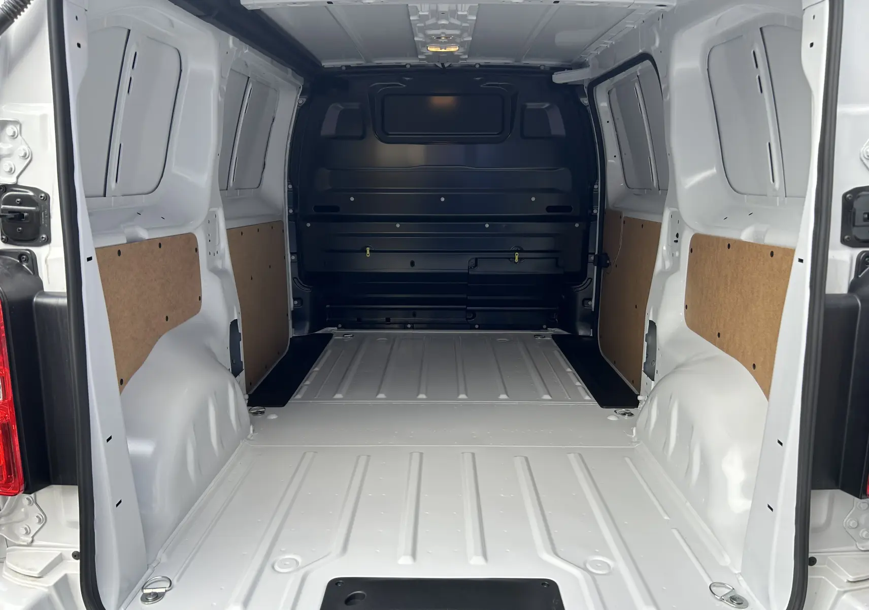 Intérieur du fourgon Citroën Jumpy blanc vu de l’arrière, montrant l’espace de chargement vide avec panneaux latéraux en bois.