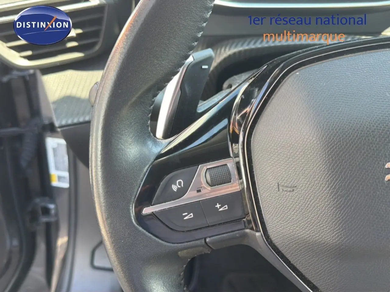 Gros plan sur le volant noir de la Peugeot 2008 1.2 PureTech 130, montrant les commandes audio et la palette de changement de vitesse.