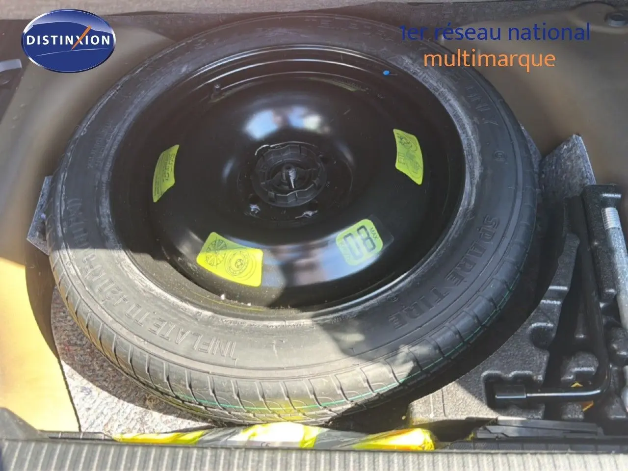 Vue plongeante sur la roue de secours noire et ses outils dans le coffre d'une Peugeot 2008 gris platinium.