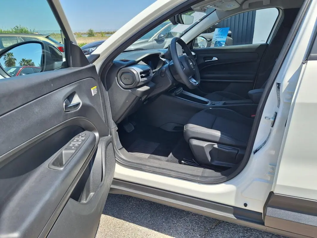 Intérieur côté conducteur du Jeep Avenger électrique blanc 2025, avec tableau de bord et sièges noirs visibles.