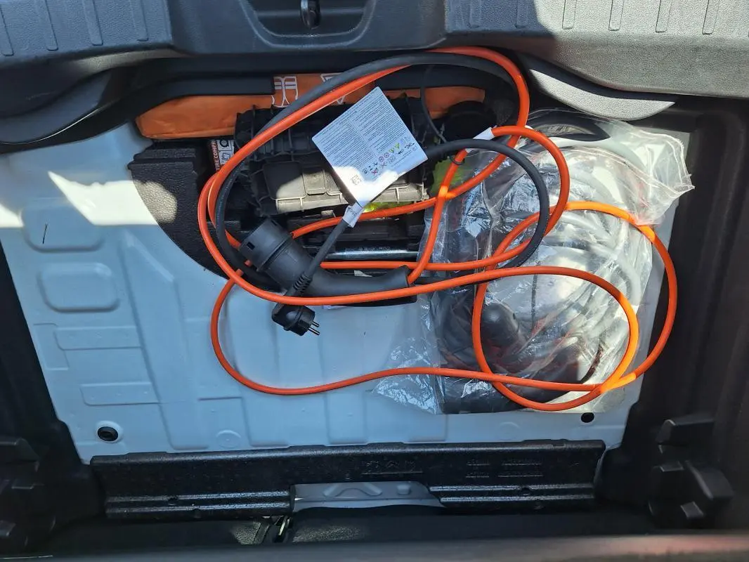 Vue du coffre ouvert d'un Jeep Avenger blanc 2025, montrant le câble de recharge électrique orange rangé.