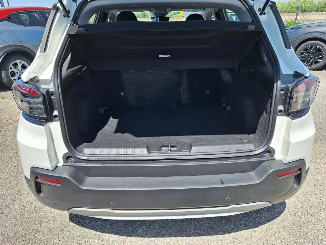 Vue arrière du coffre ouvert d'une Jeep Avenger électrique blanche, avec feux arrière et pare-chocs visibles.