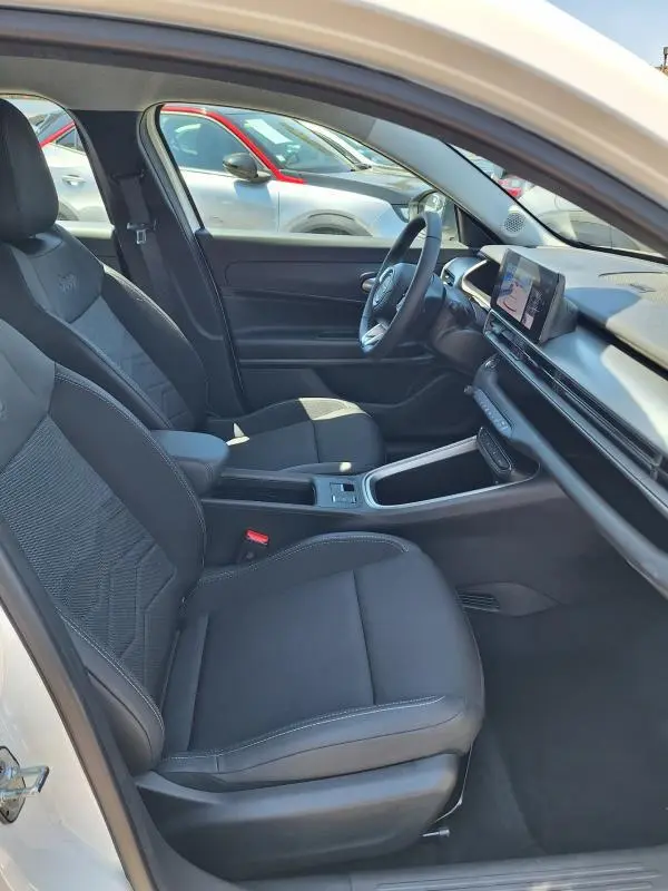 Vue intérieure côté conducteur du Jeep Avenger électrique blanc 2025, sièges noirs avec accoudoir central et écran tactile.