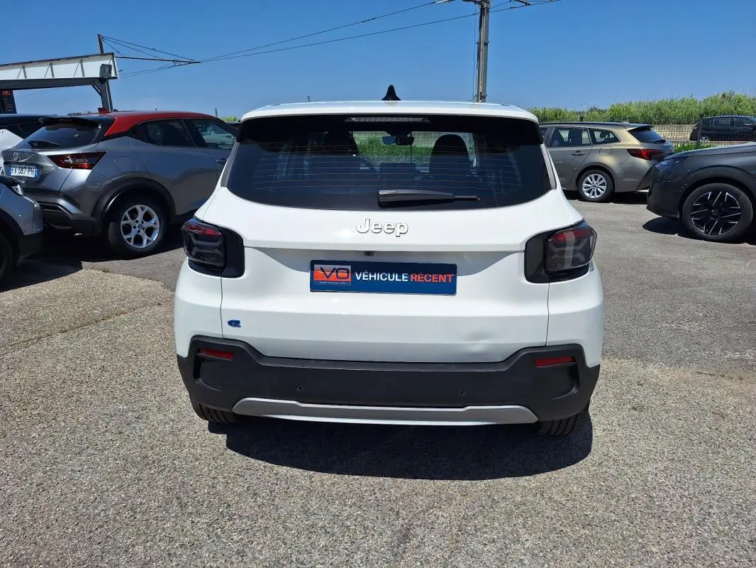 Vue arrière d'une Jeep Avenger électrique blanche 2025 avec feux arrière fumés et pare-chocs noir contrastant.