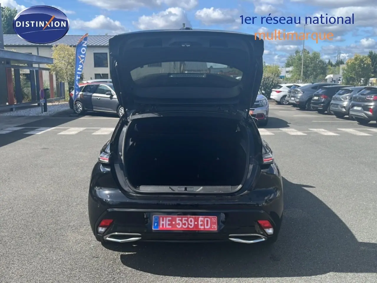 Vue arrière d'une Peugeot 308 noir métal 2025 avec coffre ouvert, stationnée sur un parking en extérieur.