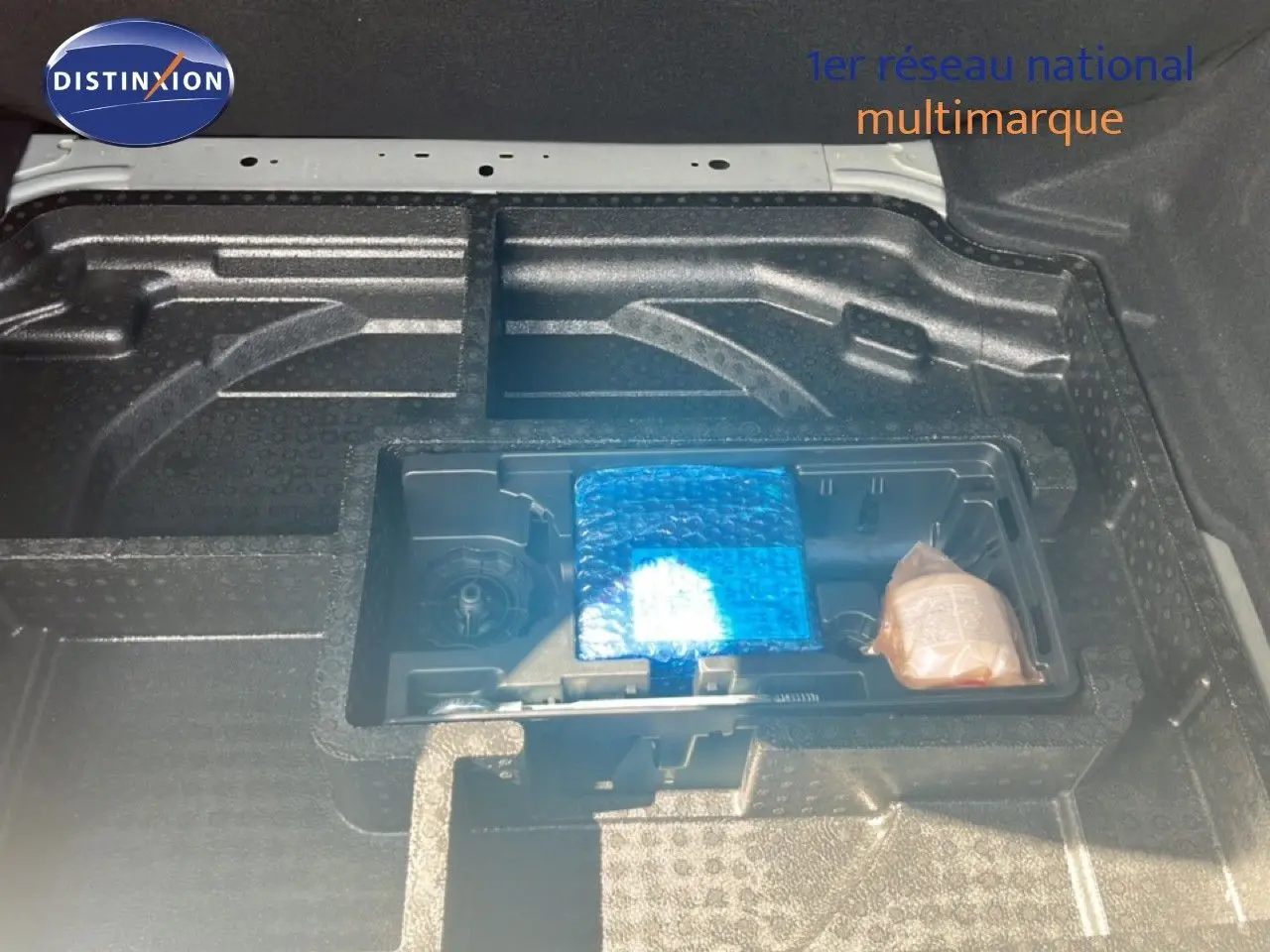 Coffre ouvert de la Peugeot 308 noir métal, vue plongeante sur le rangement sous plancher avec accessoires emballés.