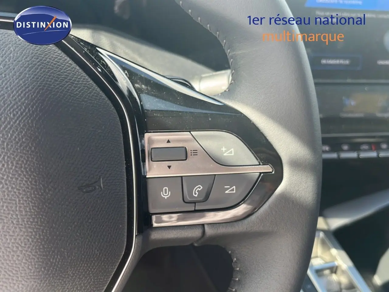Gros plan sur les commandes au volant en cuir noir de la Peugeot 308 Hybrid 2025, avec tableau de bord flou en arrière-plan.