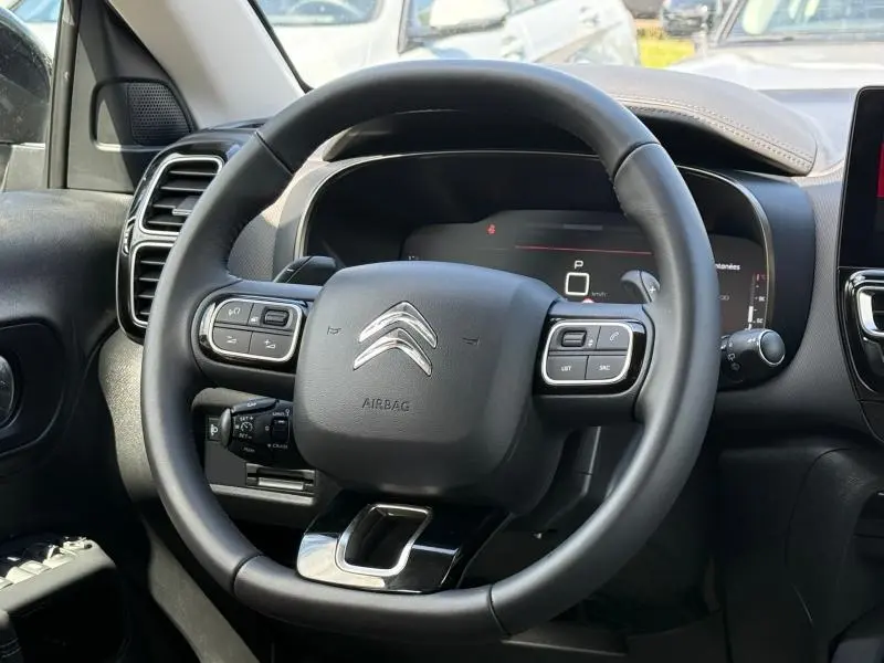 Vue rapprochée du volant cuir multifonction noir du Citroën C5 Aircross 2025 avec tableau de bord numérique en arrière-plan.