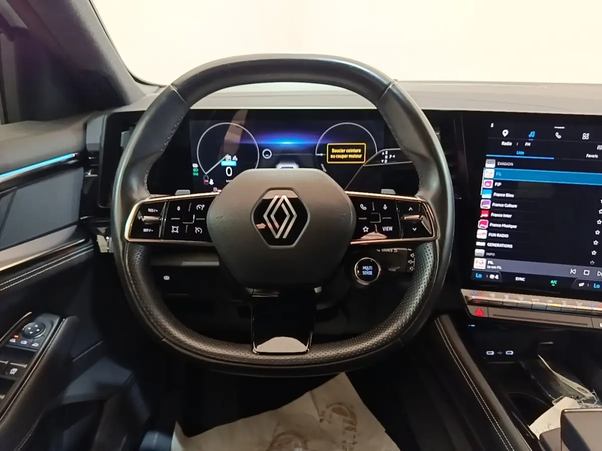 Vue centrée sur le volant cuir noir et le tableau de bord numérique du Renault Austral blanc, version hybride 2023.