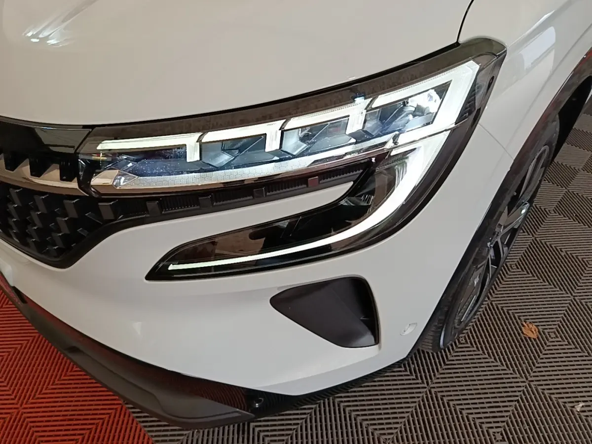Gros plan sur le phare avant droit blanc du Renault Austral Techno E-Tech Hybride 200 avec calandre noire et jante visible.