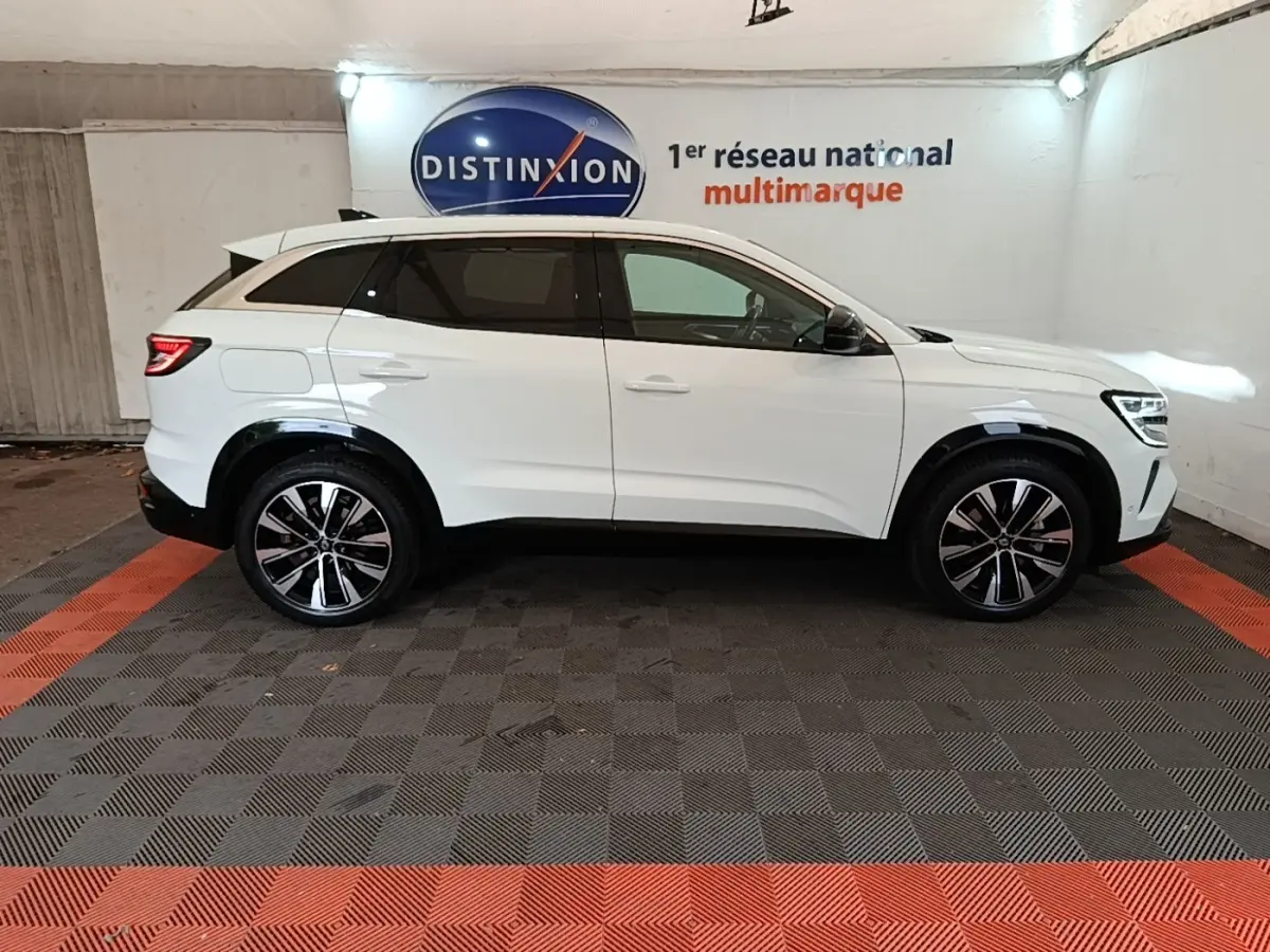 Renault Austral blanc en profil droit dans un showroom, avec jantes alliage et toit spoiler visible.