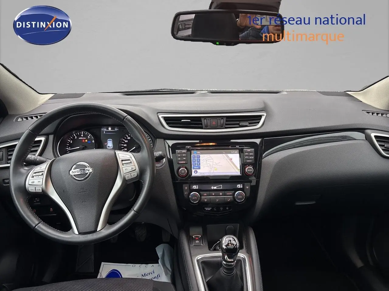Vue intérieure frontale du Nissan Qashqai blanc glacier 2017, mettant en valeur le volant, la console centrale avec écran tactile et la boîte manuelle.