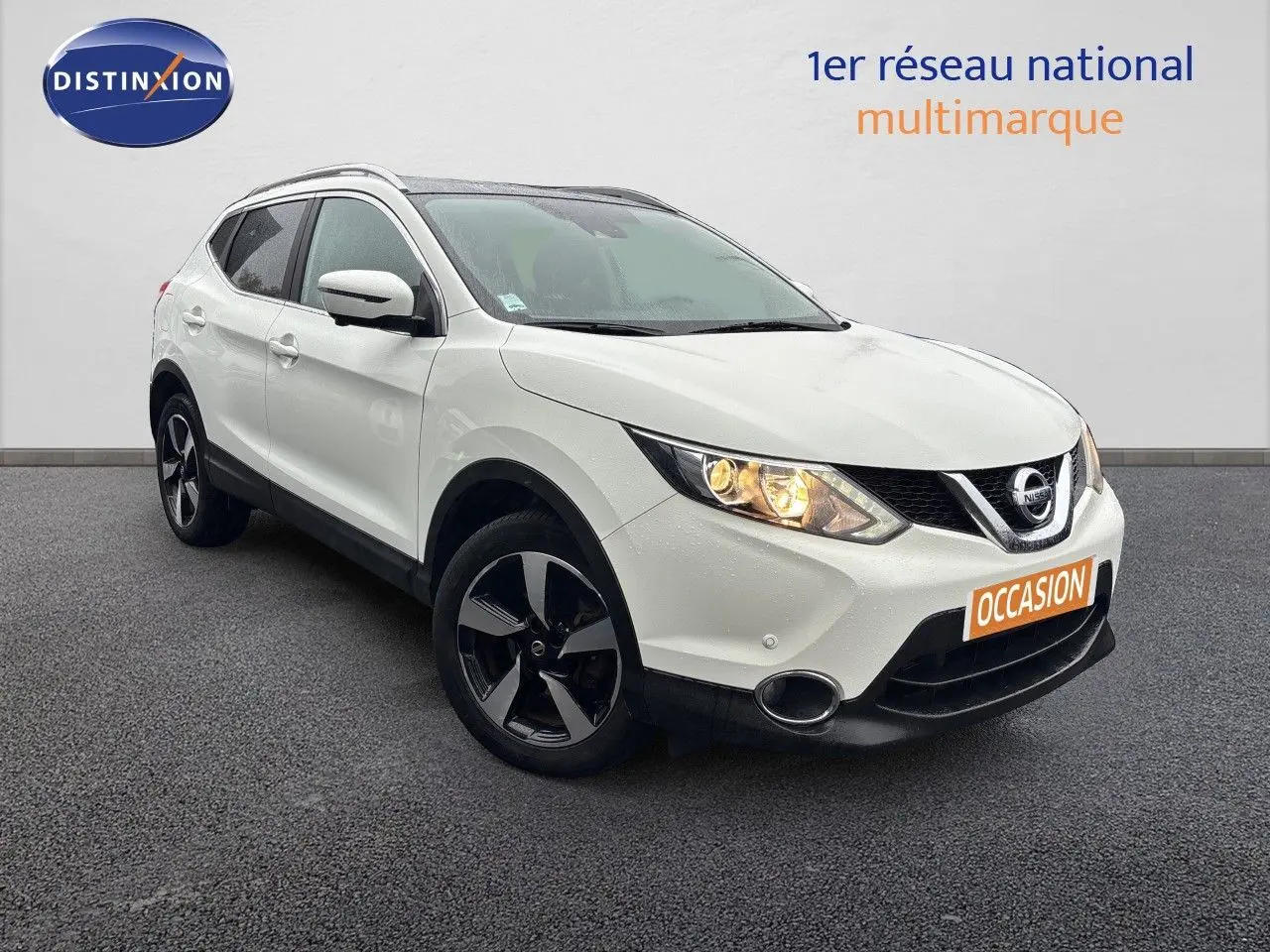 Nissan Qashqai blanc glacier en 3/4 avant droit avec jantes noires et phares allumés sur fond neutre.