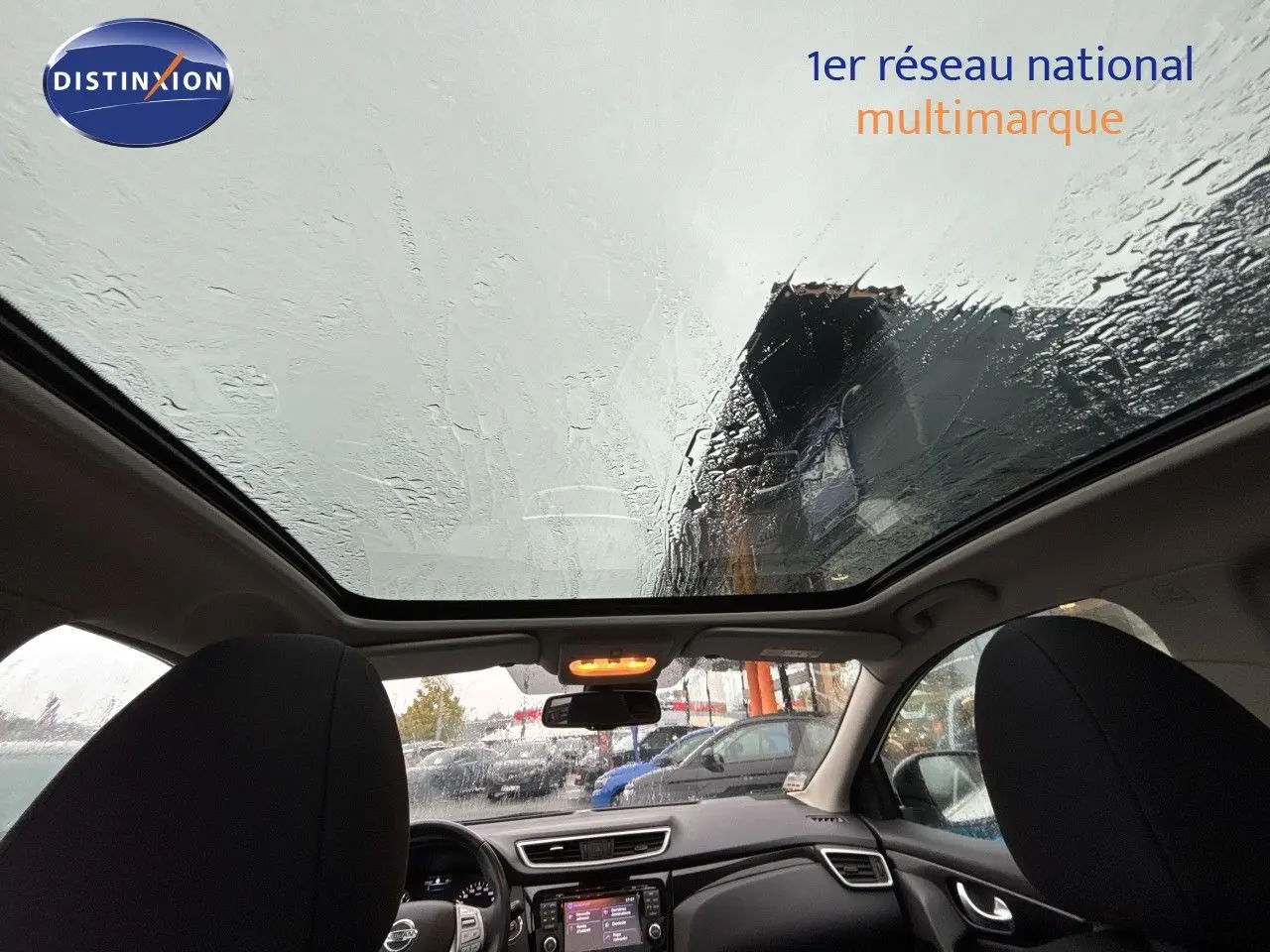 Vue intérieure avant du Nissan Qashqai blanc glacier 2017, avec toit panoramique et tableau de bord visible sous la pluie.