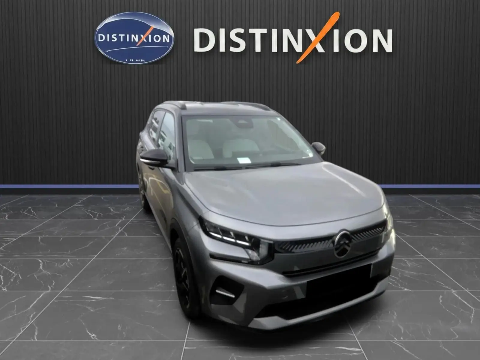 Citroën E-C3 gris en 3/4 avant droit, avec calandre noire et phares LED, sur fond intérieur showroom Distinxion.