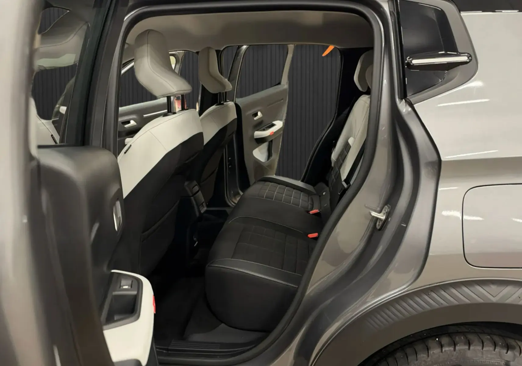 Vue intérieure arrière côté droit d'une Citroën C3 E-C3 gris 2025, sièges bicolores noir et blanc avec détails orange.