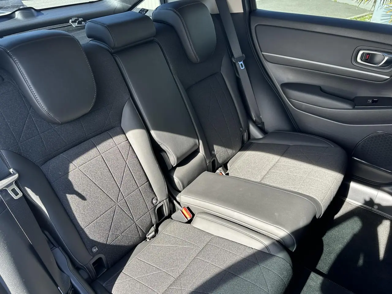 Vue intérieure arrière droite du Honda HR-V 2025 gris, montrant les sièges arrière en tissu et cuir synthétique noirs avec accoudoir central abaissé.