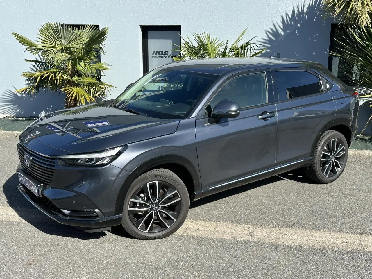 Honda HR-V gris métallisé vu de 3/4 avant droit, avec jantes alliage noires et détails modernes sur carrosserie.