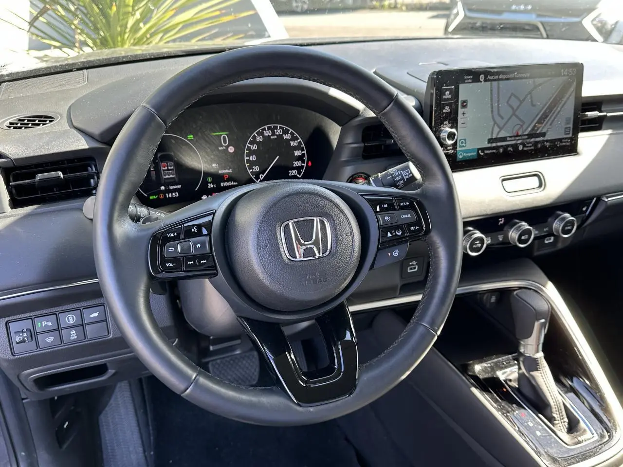 Vue intérieure centrée sur le volant cuir noir et le tableau de bord digital du Honda HR-V 2025 gris hybride.