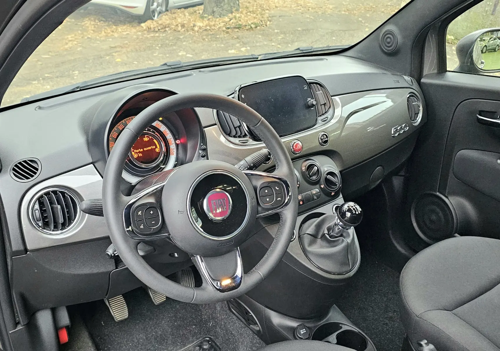 Intérieur côté conducteur de la FIAT 500 gris 2023, volant multifonction et tableau de bord moderne avec écran tactile.