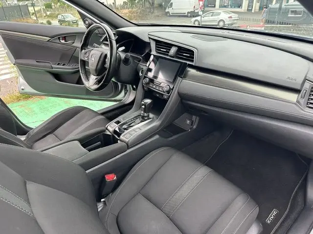 Vue intérieure côté conducteur de la Honda Civic grise, avec tableau de bord moderne et volant cuir noir.
