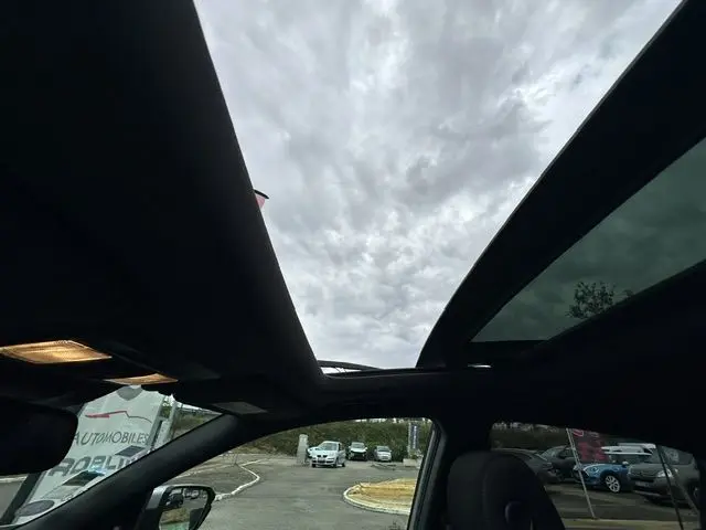 Vue intérieure du toit ouvrant panoramique d'une Honda Accord grise, avec ciel nuageux visible à travers le verre.